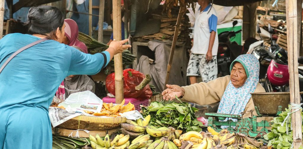Seorang perempuan membeli produk lokal dari pedagang di pasar tradisional.