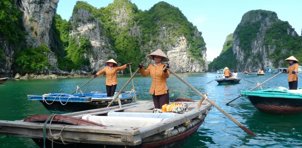 tiga nelayan berbaju coklat berdiri di atas perahu mereka masing-masing di Teluk Halong, Vietnam