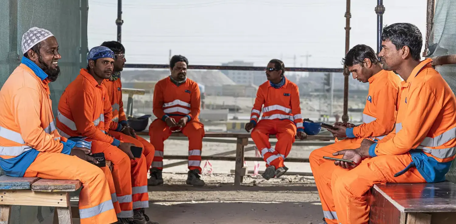 enam pekerja Piala Dunia Qatar dalam seragam oranye duduk bersama-sama