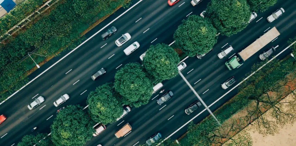 sejumlah mobil melintas di jalanan dengan pepohonan di kiri, kanan, dan tengah jalan.