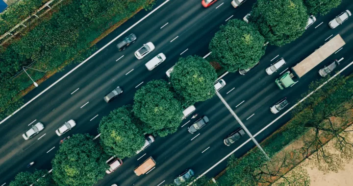 sejumlah mobil melintas di jalanan dengan pepohonan di kiri, kanan, dan tengah jalan.