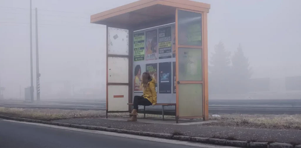 seorang perempuan duduk di tempat penghentian bus dengan asap di sekelilingnya