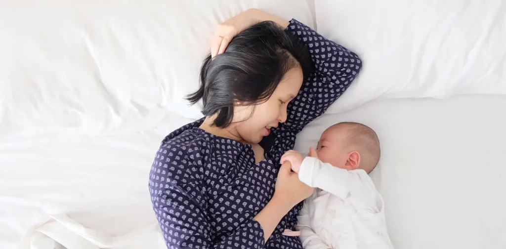 seorang perempuan memperhatikan dan memegang tangan bayinya di atas kasur
