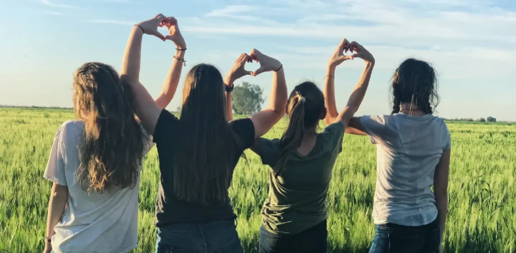 empat perempuan saling menyatukan tangan membentuk tanda cinta di tengah hamparan sawah.