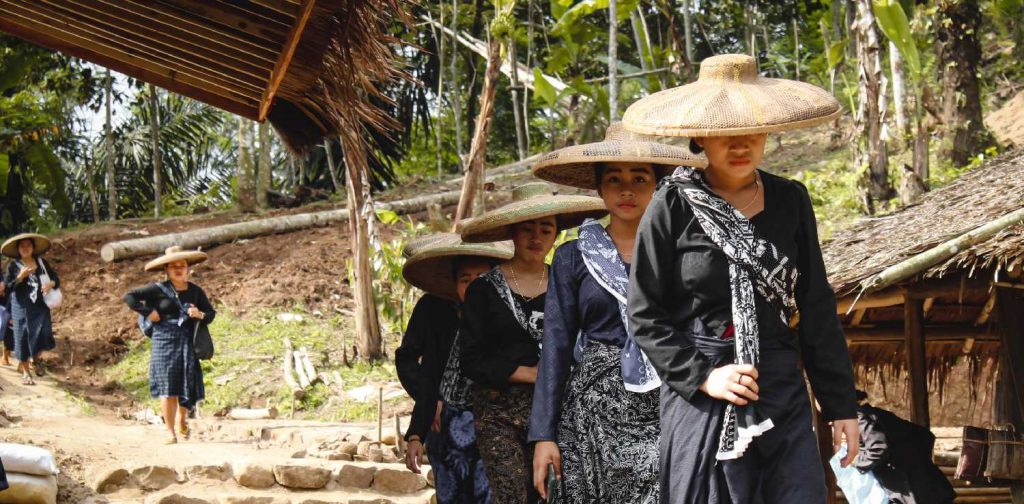 lima perempuan mengenakan pakaian adat suku baduy berjalan beriringan.