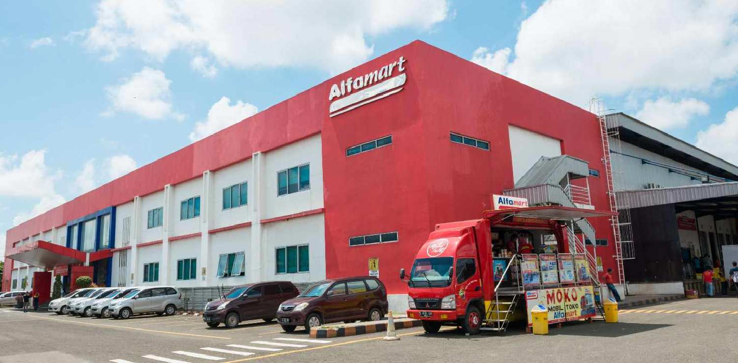 Sejumlah mobil terparkir di halaman kantor Alfamart dengan satu mobil toko (moko) Alfamart di sebelah kanan.