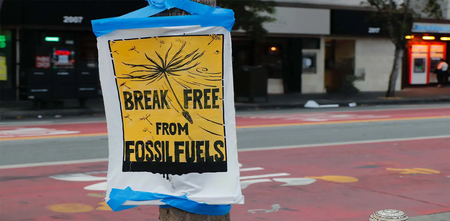 tanda kuning bertuliskan “Break Free from Fossil Fuels” terpampang di tiang lampu.