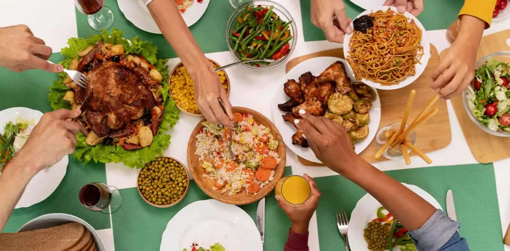 hidangan berbagai makanan di atas meja dengan tangan-tangan yang sedang menciduk.