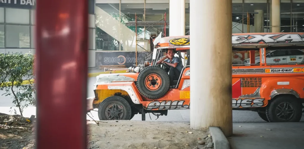 sebuah jeepney berwarna oranye dengan sopir di dalamnya