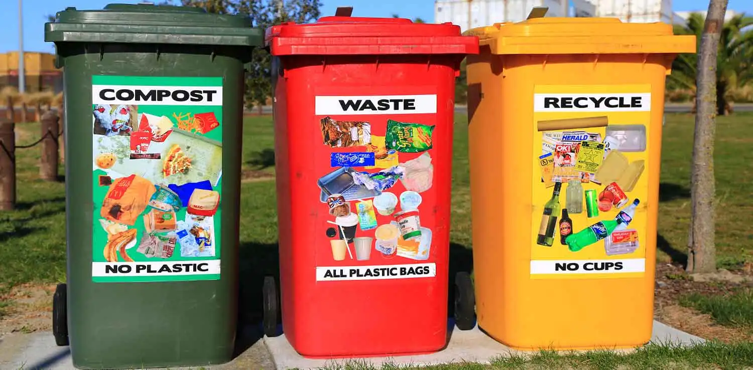 Tiga tempat sampah besar berwarna hijau, merah, dan kuning untuk kompos, limbah, dan daur ulang