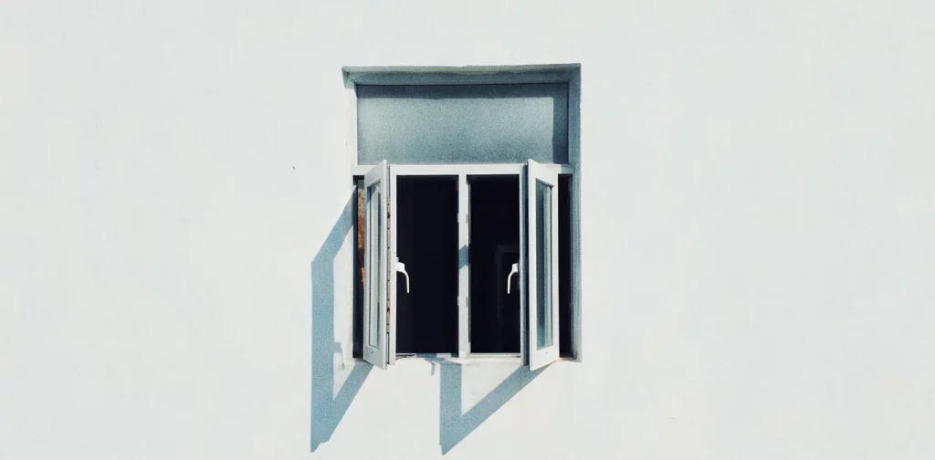 sebuah jendela yang terbuka dengan di tengah dinding putih