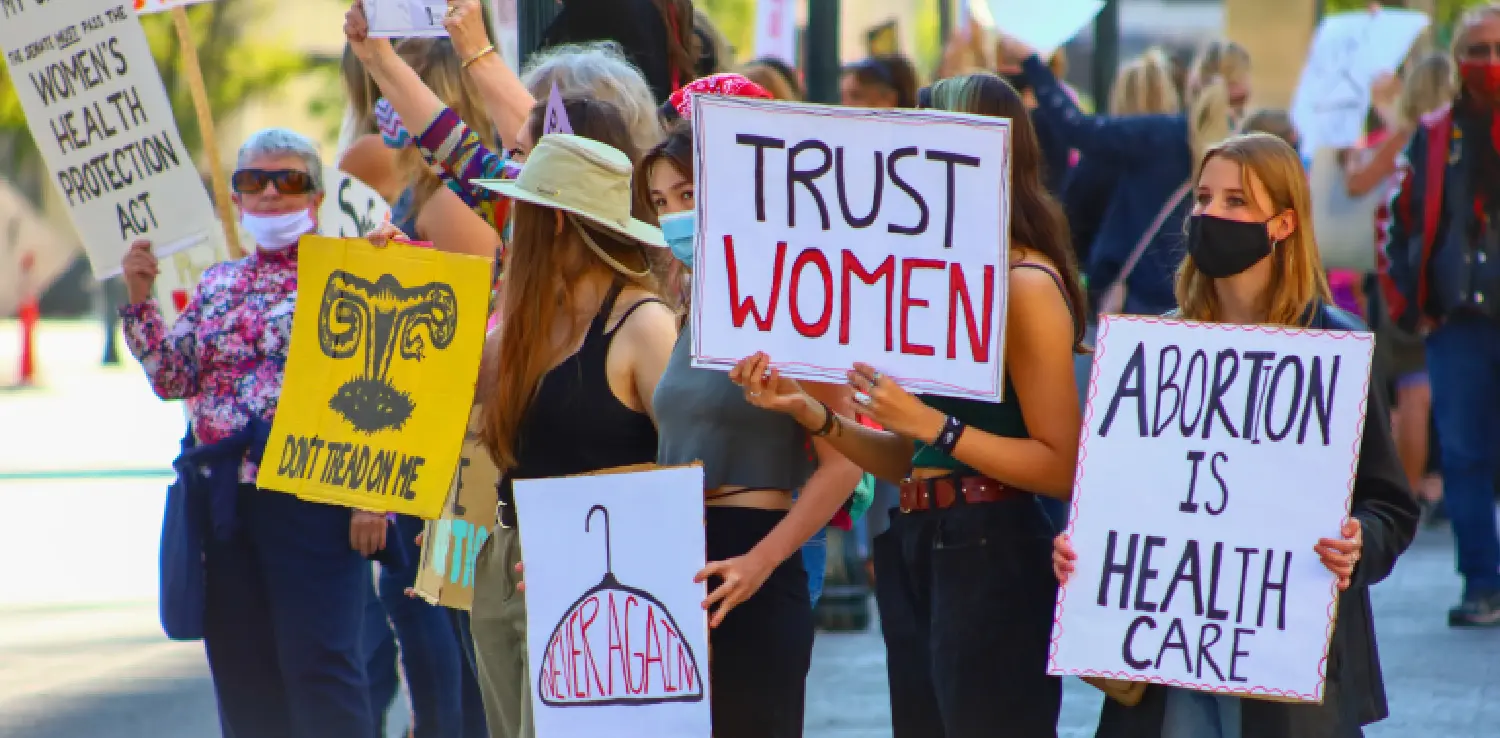 sekelompok perempuan berbaris sambil menunjukkan pesan melalui poster