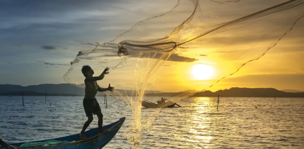 Seorang nelayan dengan perahu kecil menebar jala dengan matahari menggantung di cakrawala.