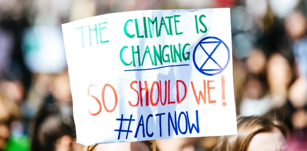 Sepasang tangan memegang poster bertuliskan “The Climate Is Changing. So Should We #Actnow”.