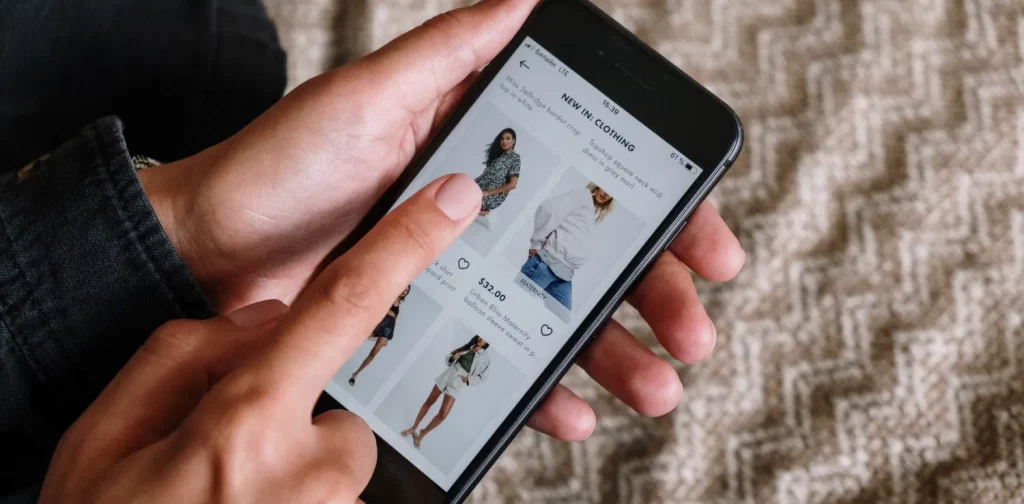 seseorang menunjuk ke layar ponsel yang menampilkan pilihan dari toko pakaian online
