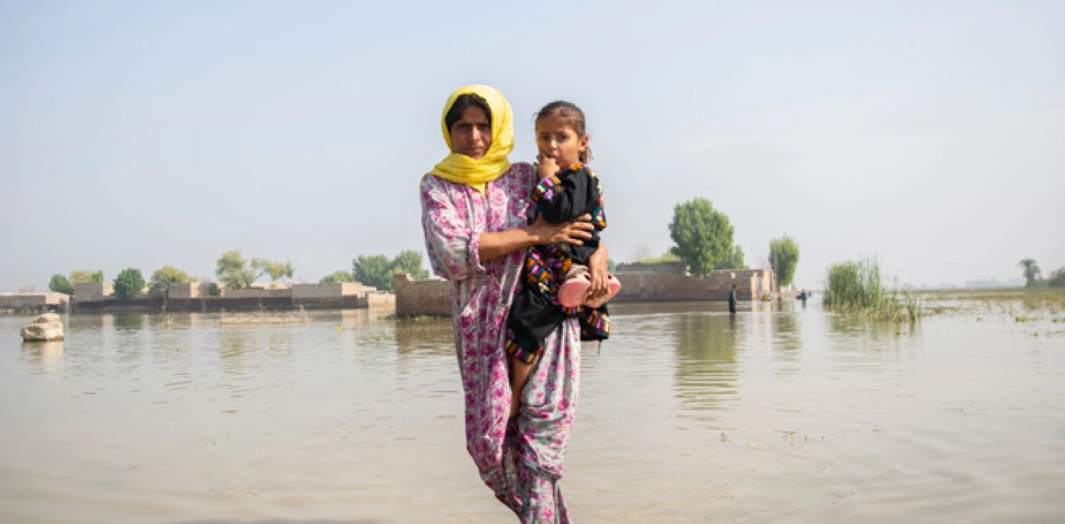 seorang perempuan berkerudung menggendong anak dengan latar genangan air.