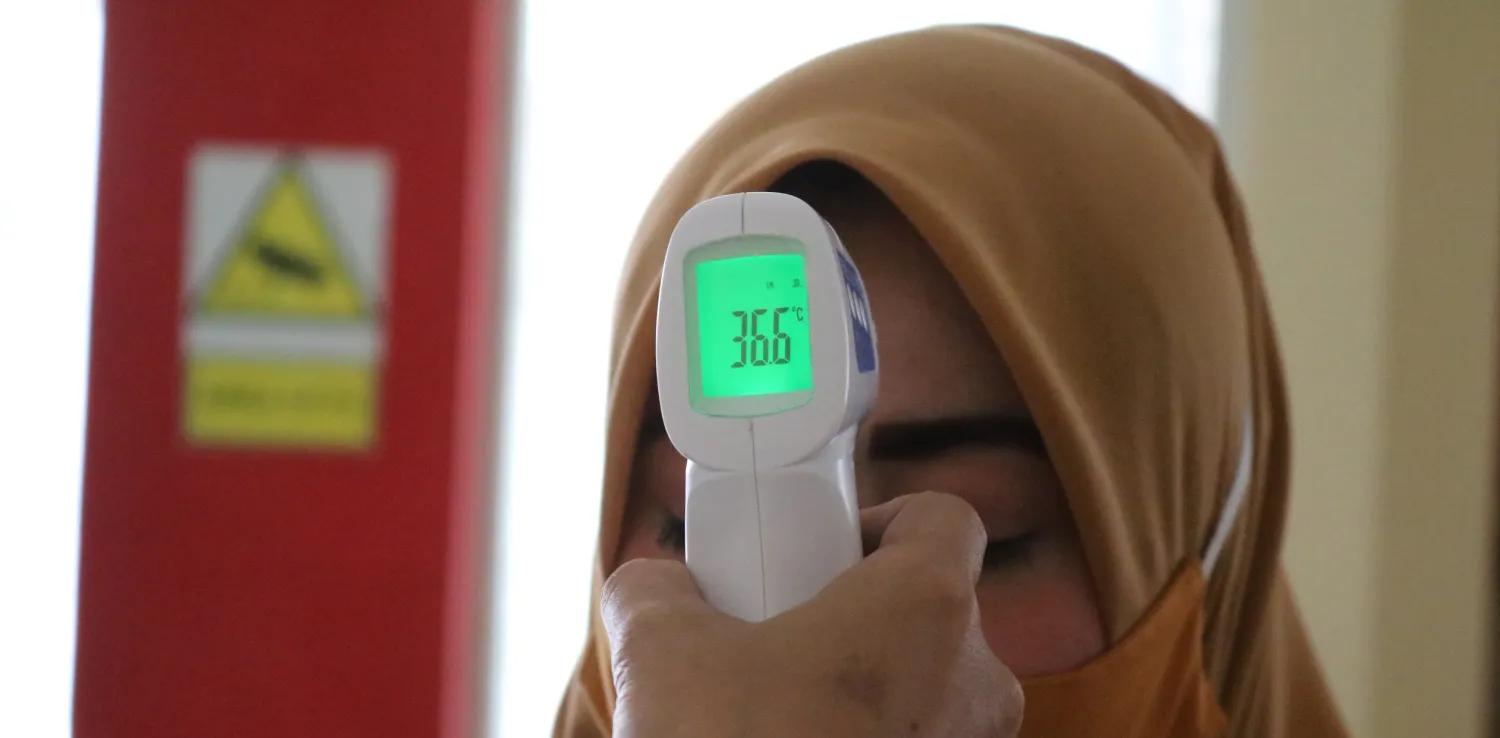 seorang perempuan menjalani pemeriksaan suhu tubuh oleh seorang tenaga kesehatan.