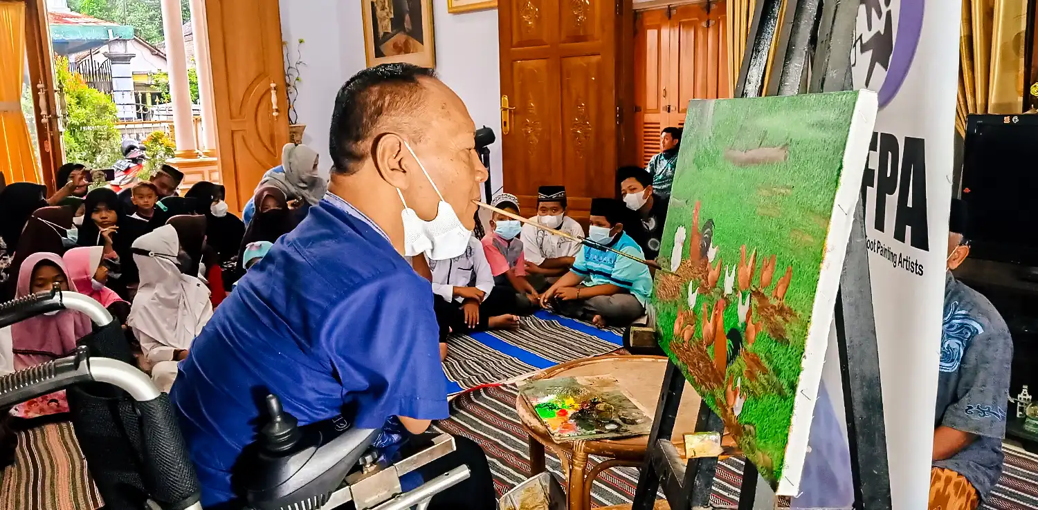 seorang pria melukis dengan kuas di mulut dengan anak-anak di sekelilingnya.