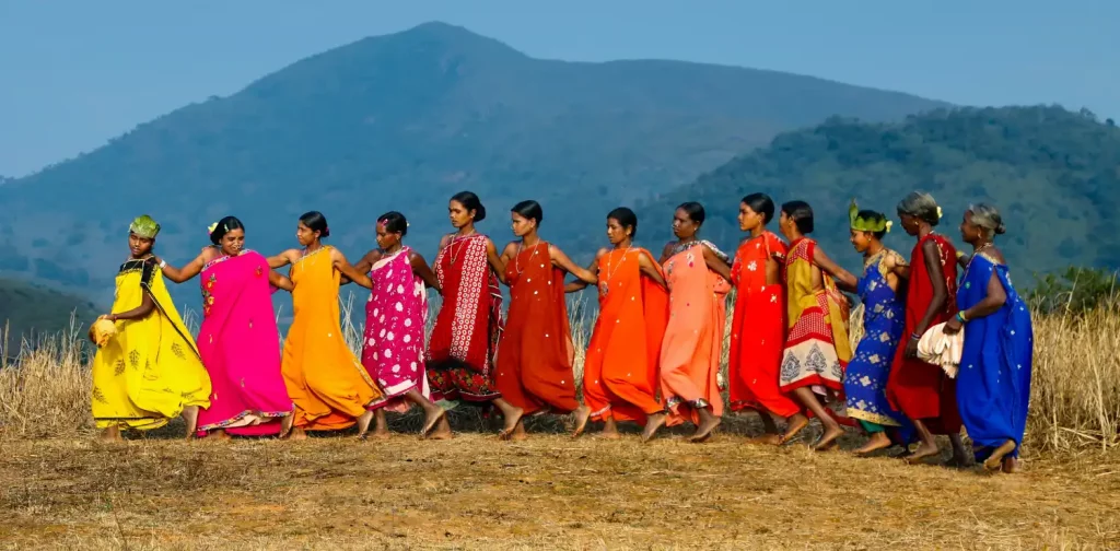 sekelompok perempuan adat saling bergandengan tangan di hamparan lahan kosong dengan latar perbukitan.