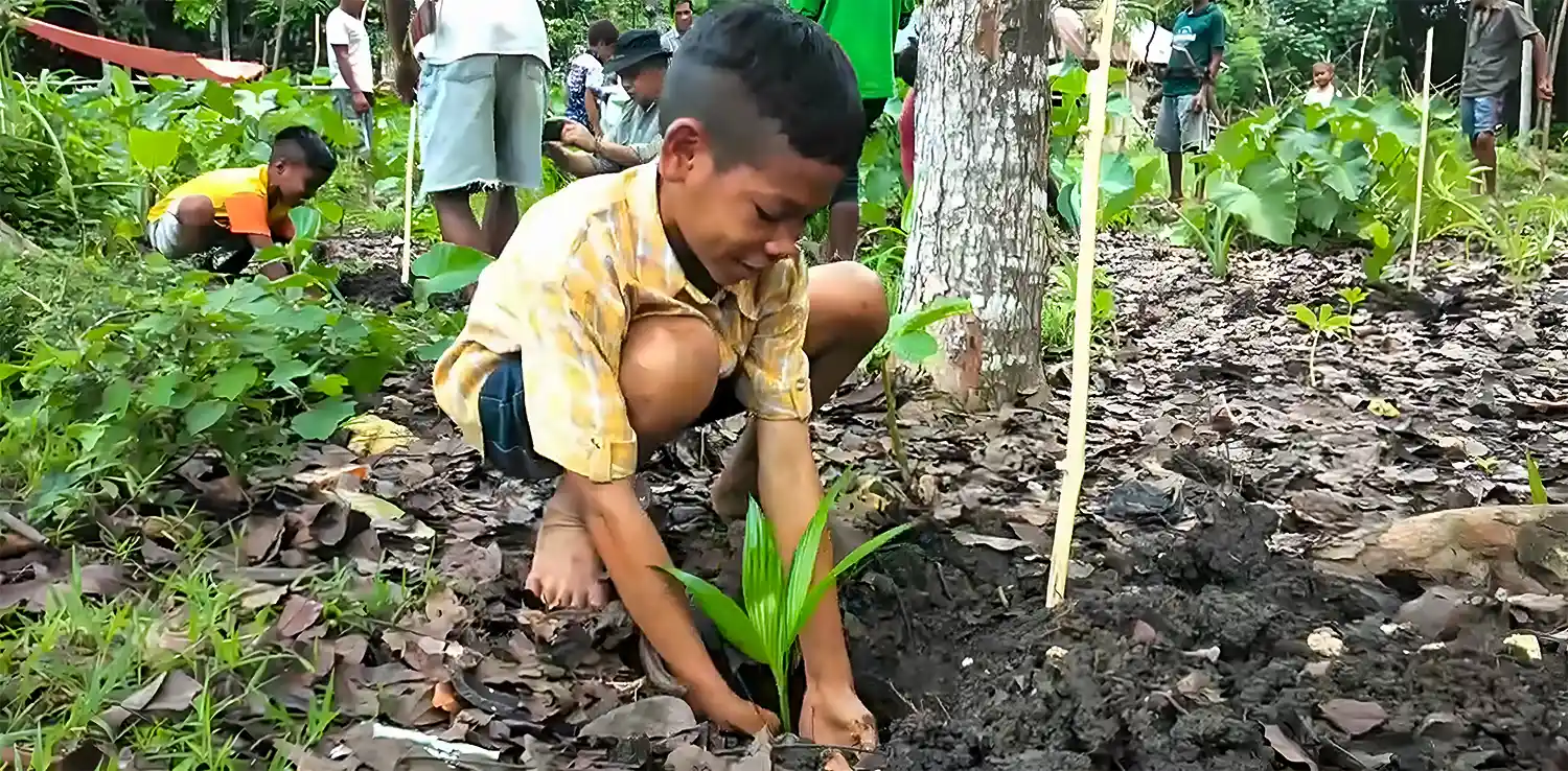 seorang anak memasukkan bibit pohon ke dalam lubang di tanah.