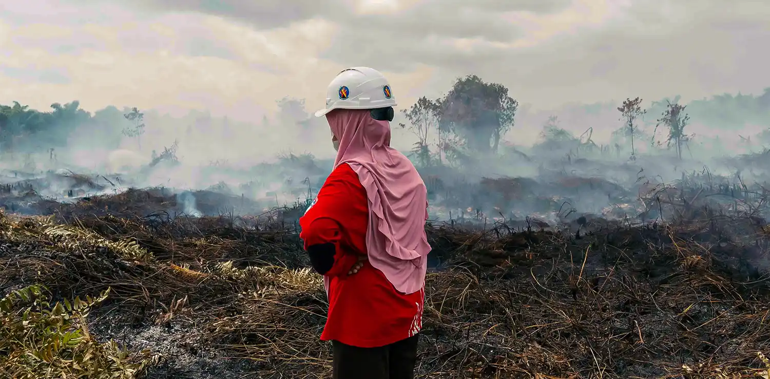Seorang perempuan berdiri di dekat lahan hutan yang terbakar.