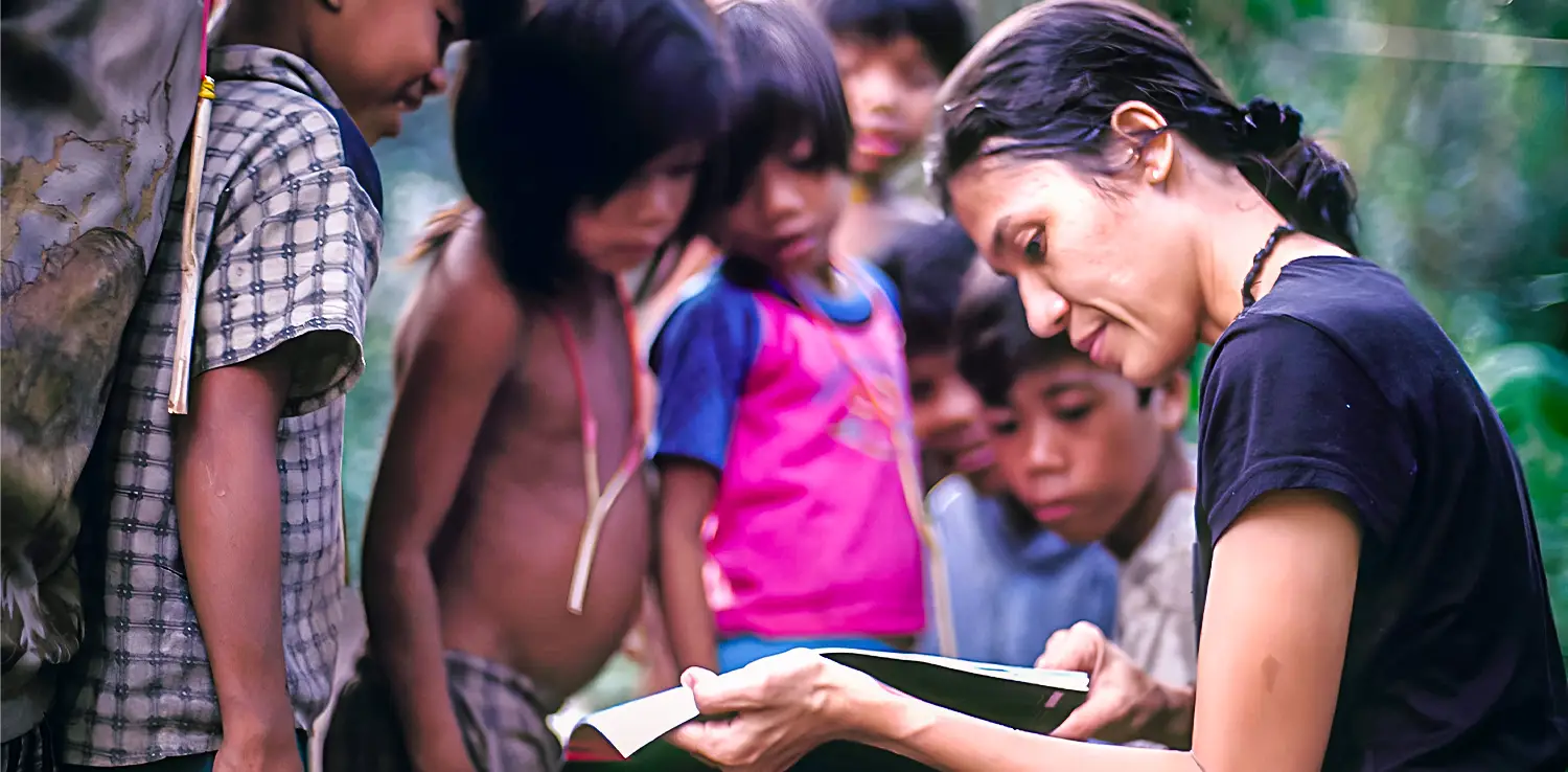 seorang perempuan sedang memegang buku dan mengajari anak-anak kecil.