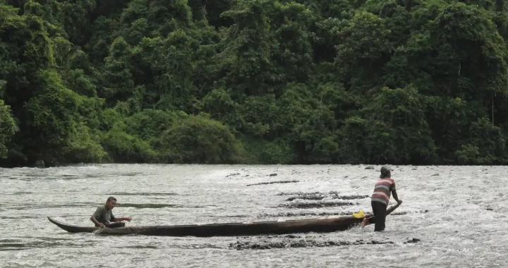 dua pria di tengah sungai dengan perahu kayu.