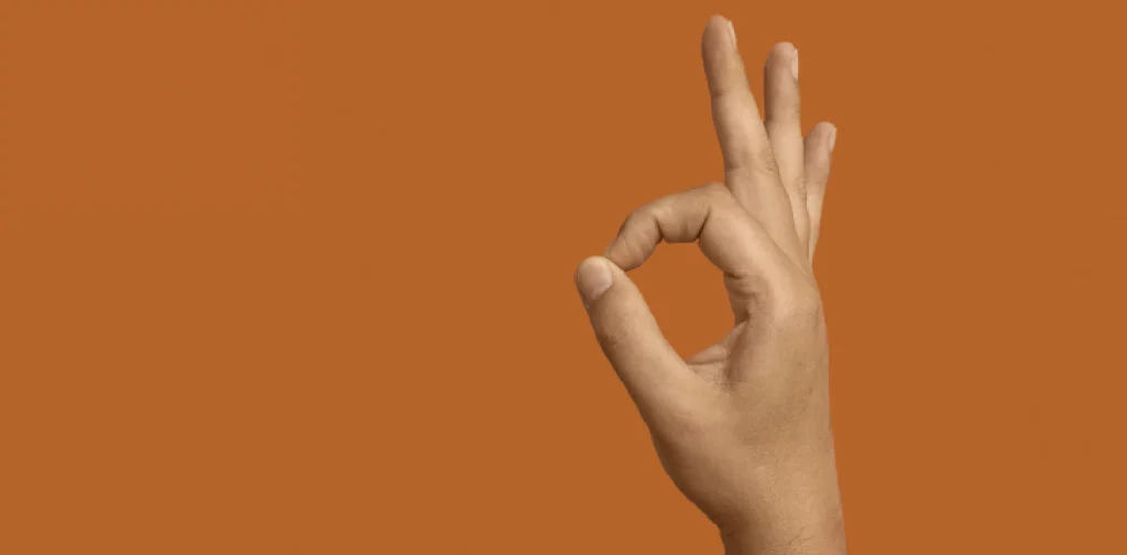 sebuah tangan melakukan pose OK dengan latar belakang oranye