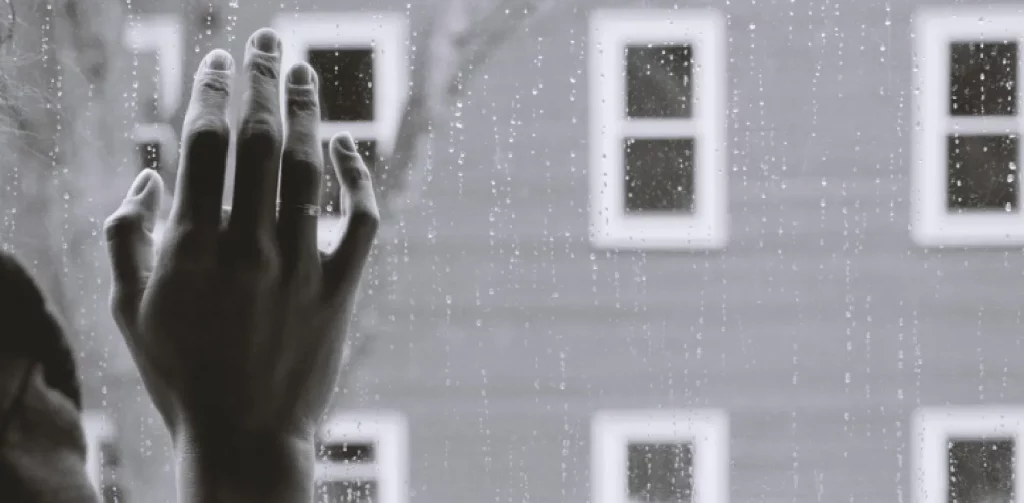 sebuah tangan menyentuh kaca jendela yang berintik air