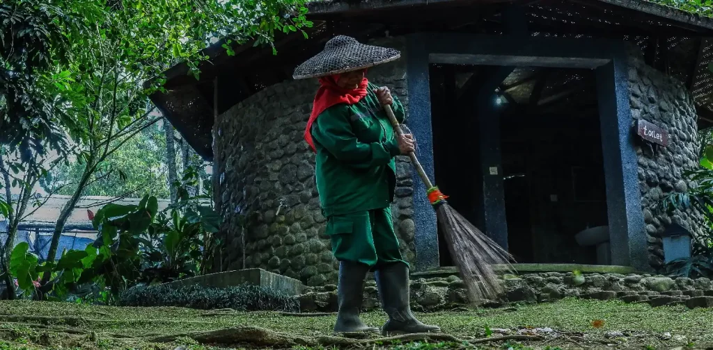 seorang perempuan bertopi sedang menyapu halaman