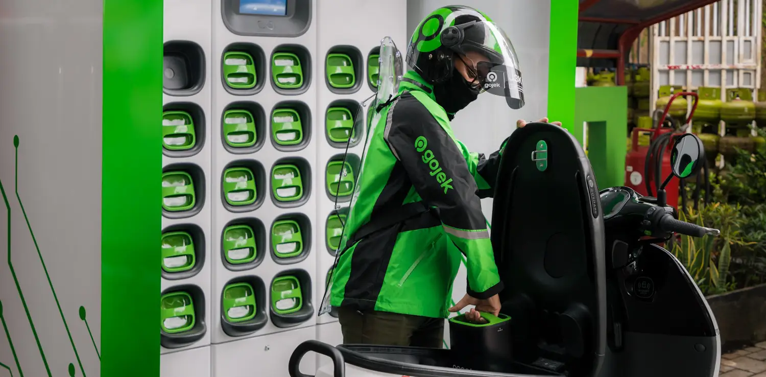seorang pengemudi ojek online sedang mengganti aki sepeda motor listriknya