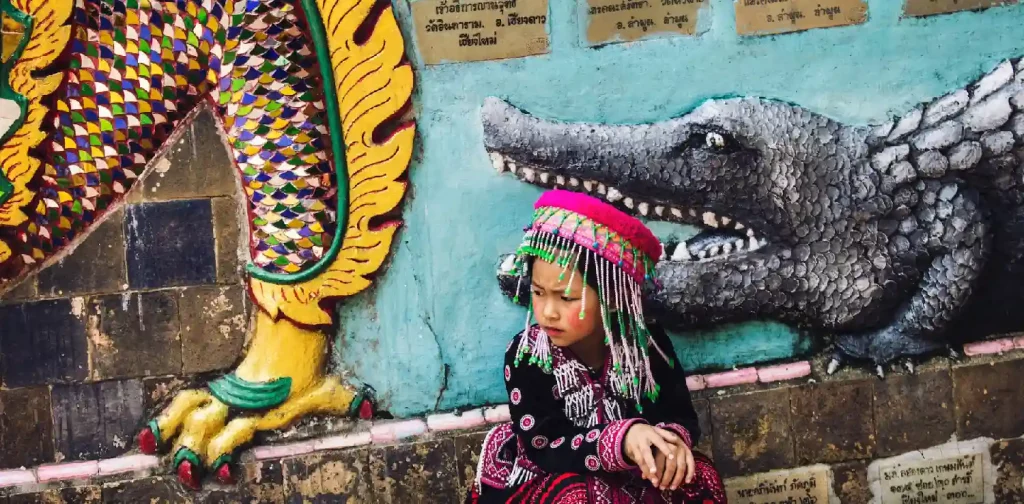 gadis kecil berpakaian tradisional Thailand di depan dinding dengan mural buaya