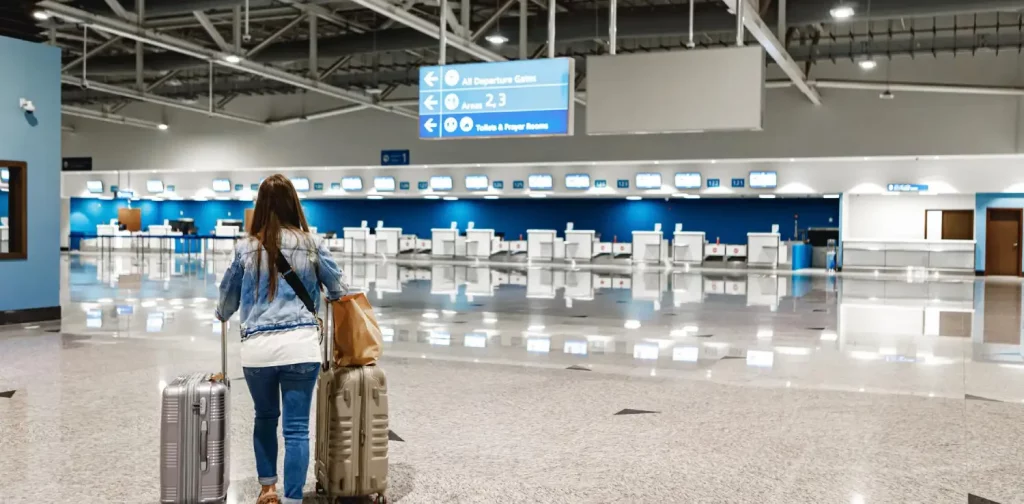 seorang perempuan berjalan di bandara dengan membawa dua koper.