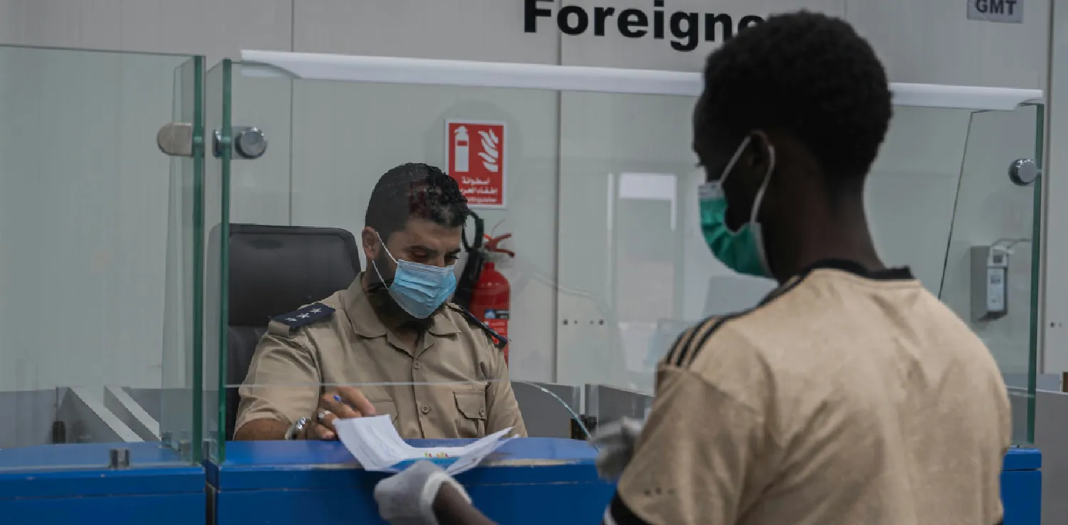 seorang pria menyerahkan paspor dan dokumen migrasi kepada petugas di belakang konter
