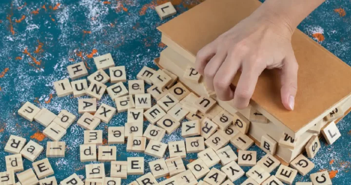 dadu-dadu kayu bertuliskan huruf-huruf dengan sebuah tangan memegang sebuah buku