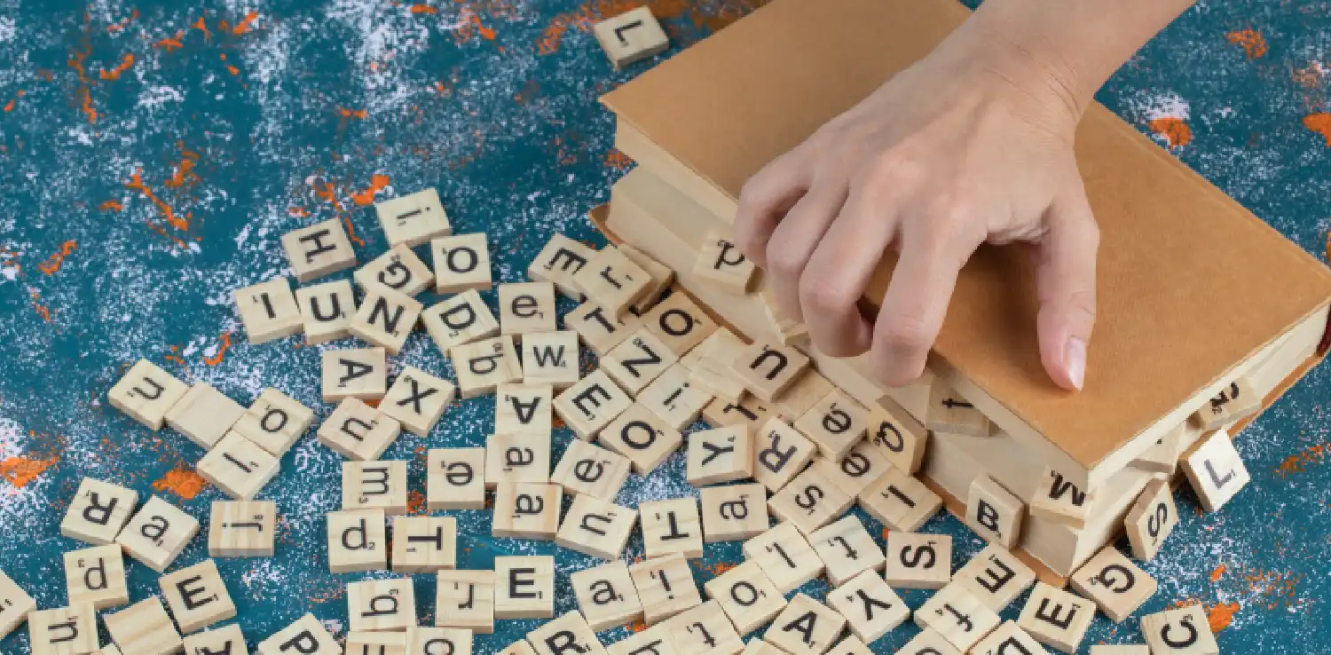 dadu-dadu kayu bertuliskan huruf-huruf dengan sebuah tangan memegang sebuah buku