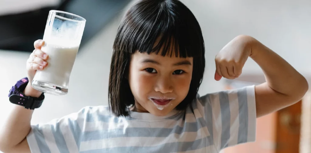 seorang anak perempuan memegang gelas berisi cairan putih seperti susu dan mulutnya belepotan susu.