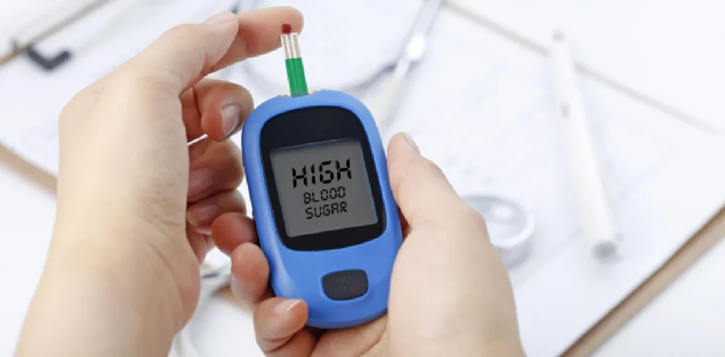 sepasang tangan memegang alat glukometer dengan tulisan ‘high blood sugar’ pada layar.
