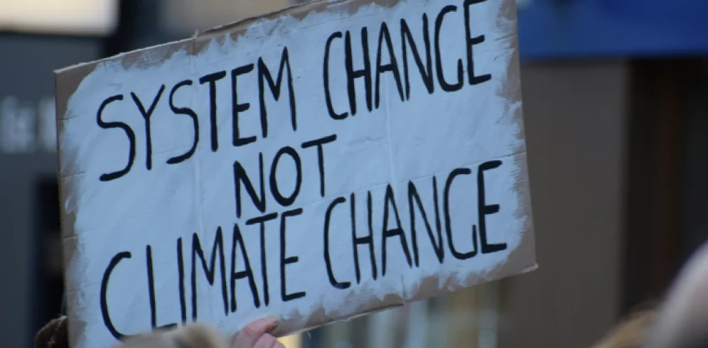 tangan yang memegang spanduk bertuliskan ‘system change not climate change’