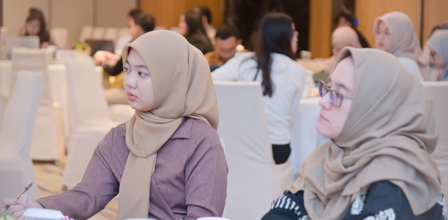 dua perempuan duduk di kursi sedang menyimak pemaparan.