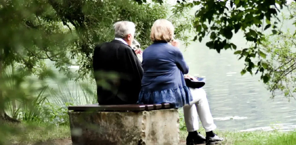 sepasang lansia duduk di tepi danau