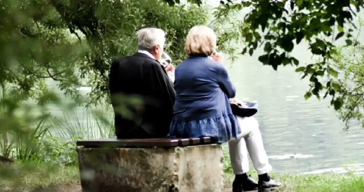 sepasang lansia duduk di tepi danau