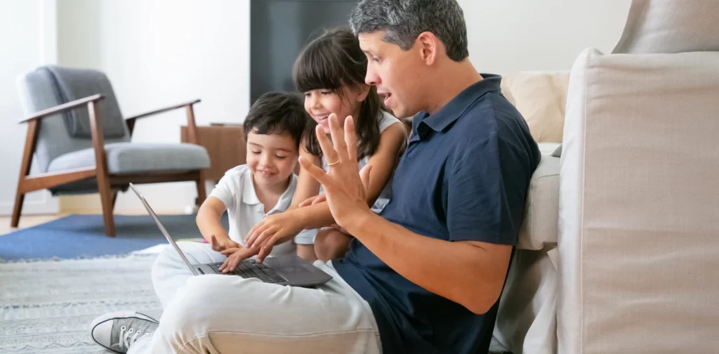 seorang pria bersama dua anak melihat layar laptop bersama.