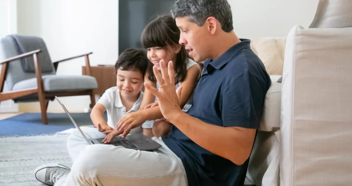 seorang pria bersama dua anak melihat layar laptop bersama.