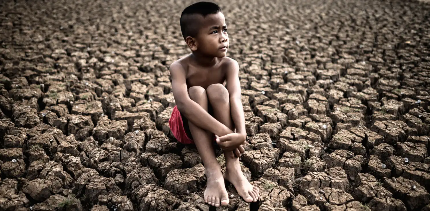 Seorang anak laki-laki duduk di atas tanah yang kering tandus.