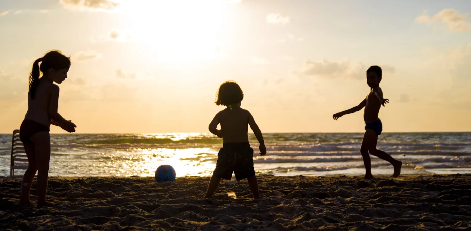 Tiga orang anak sedang bermain bola di pantai.