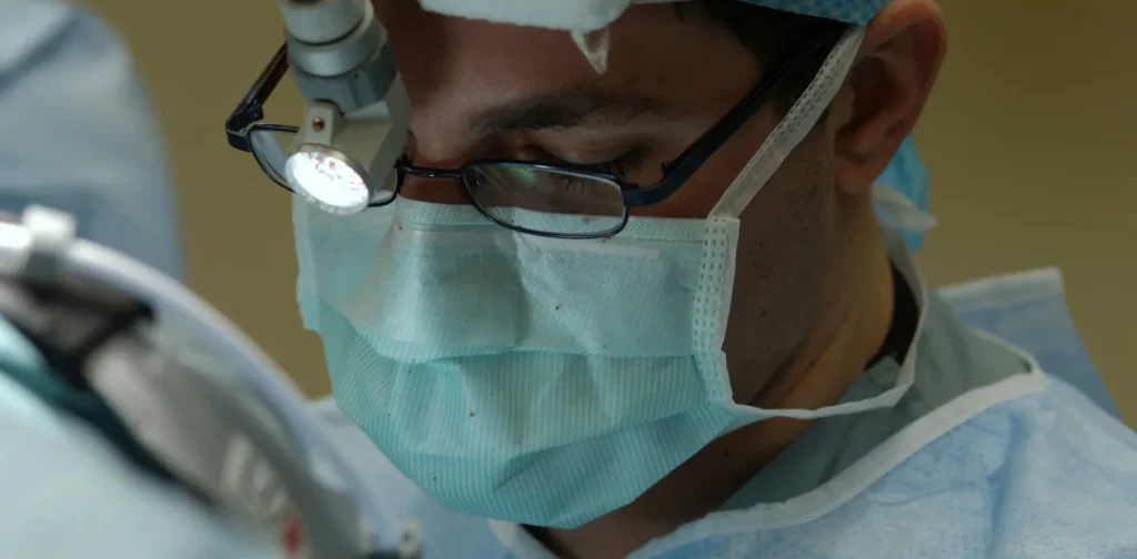 foto jarak dekat seorang dokter yang memakai scrub dan masker sedang melakukan operasi