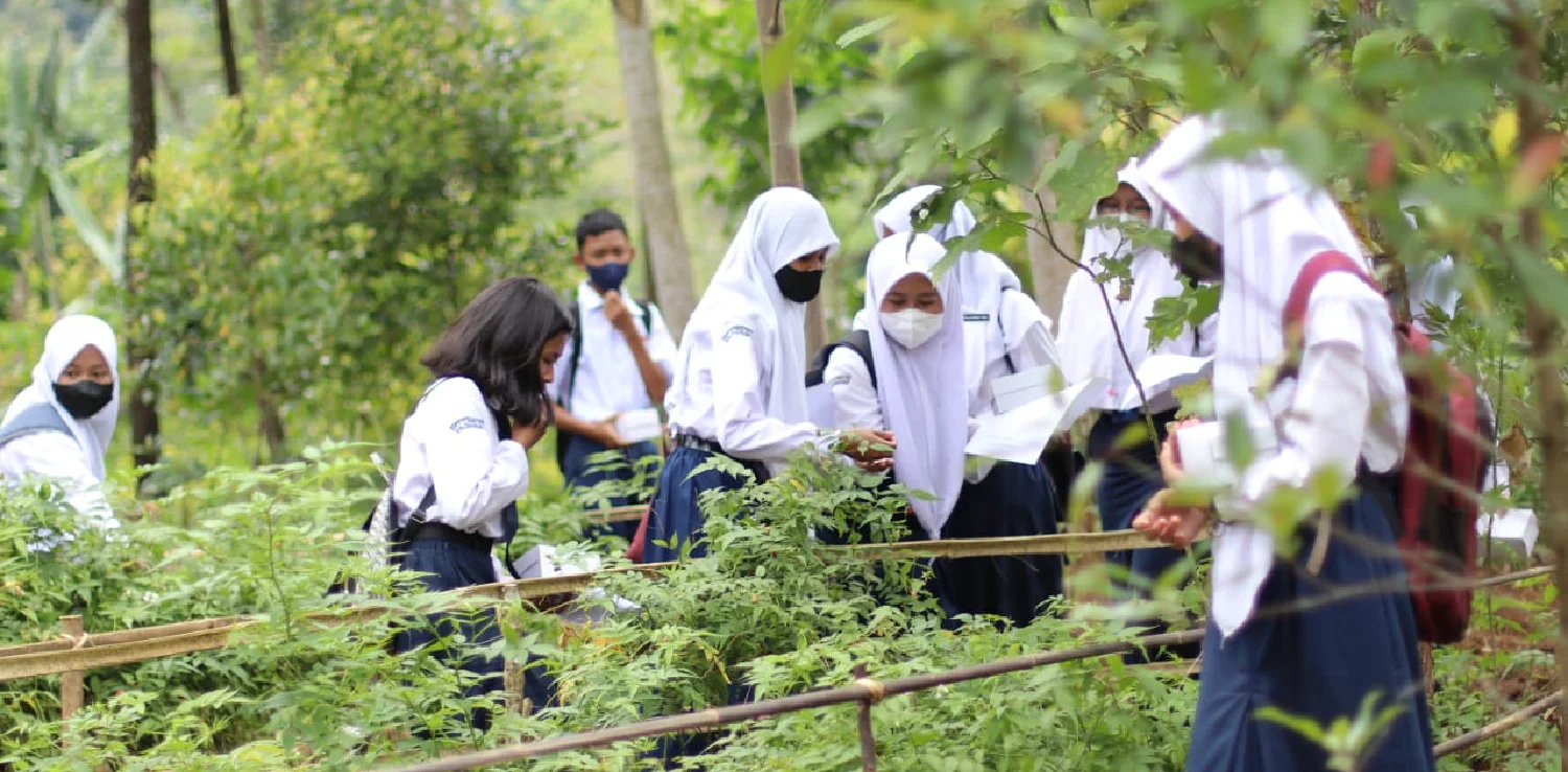 Beberapa siswa dan siswi SMP di antara pepohonan dan tanaman di kebun
