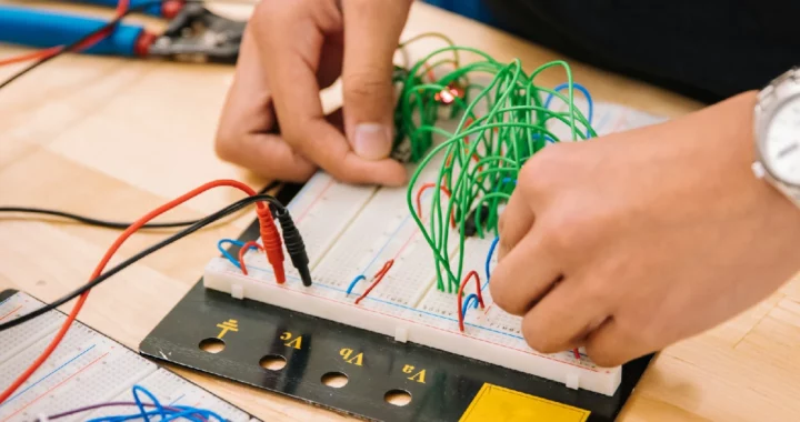 Sepasang tangan sedang mengerjakan rangkaian berbagai warna kabel, difoto dari dekat