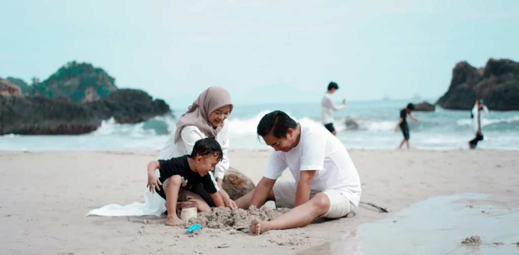satu keluarga terdiri dari ayah, ibu, dan anak bermain pasir di pantai